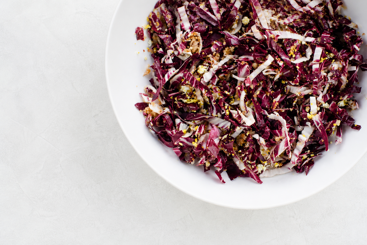 Overhead view of shredded burgundy radicchio with golden breadcrumbs and sieved egg in a white bowl